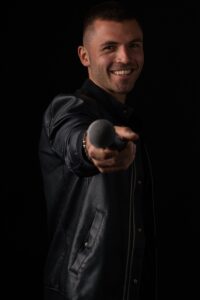 Confident singer smiling and pointing a microphone in a stylish black leather jacket.